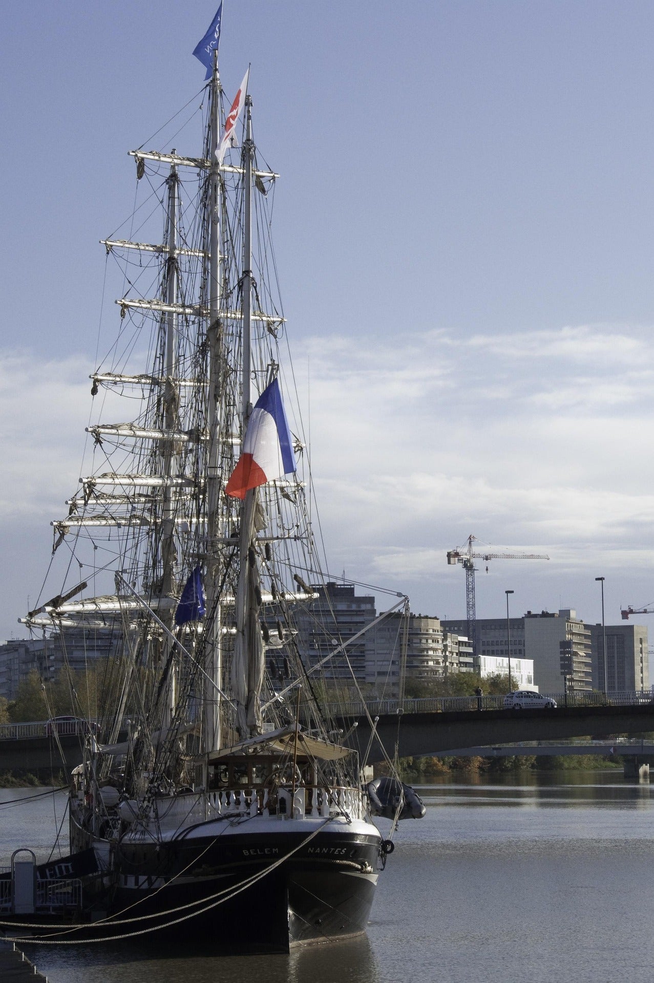 Voilier amarré à Nantes avec drapeau français, illustrant la page FAQ sur les livraisons d’objets publicitaires en France, en Corse et dans les territoires d’outre-mer.